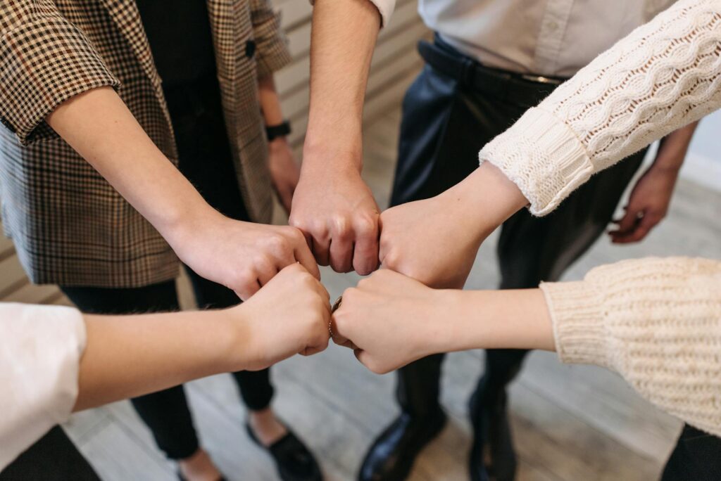 Five people uniting hands indoors, symbolizing teamwork and unity.